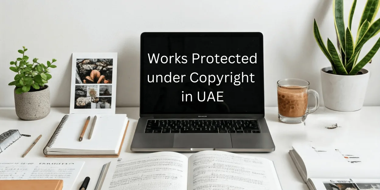 A workspace featuring a laptop displaying 'Works Protected under Copyright in UAE', with an open book, notebook with pen, framed photo, coffee cup, and potted plants.